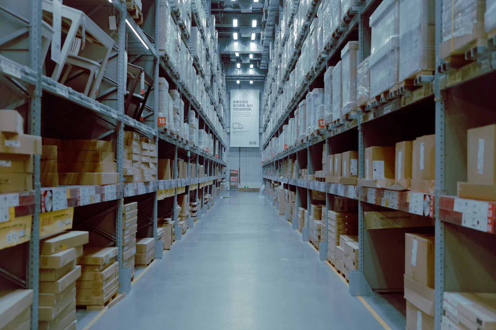 A long warehouse aisle lined with tall shelves of boxed stock